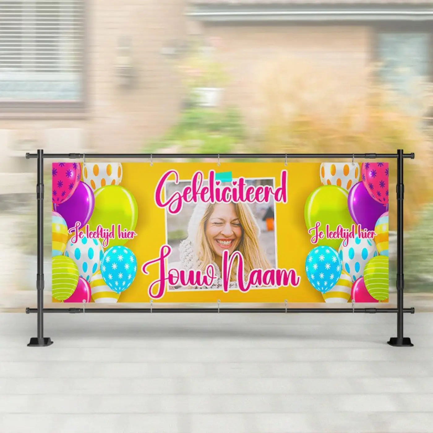 Gele spandoek verjaardag met ballonnen en foto met roze tekst gelukkig verjaardag en jouw naam aan zwarte stangen